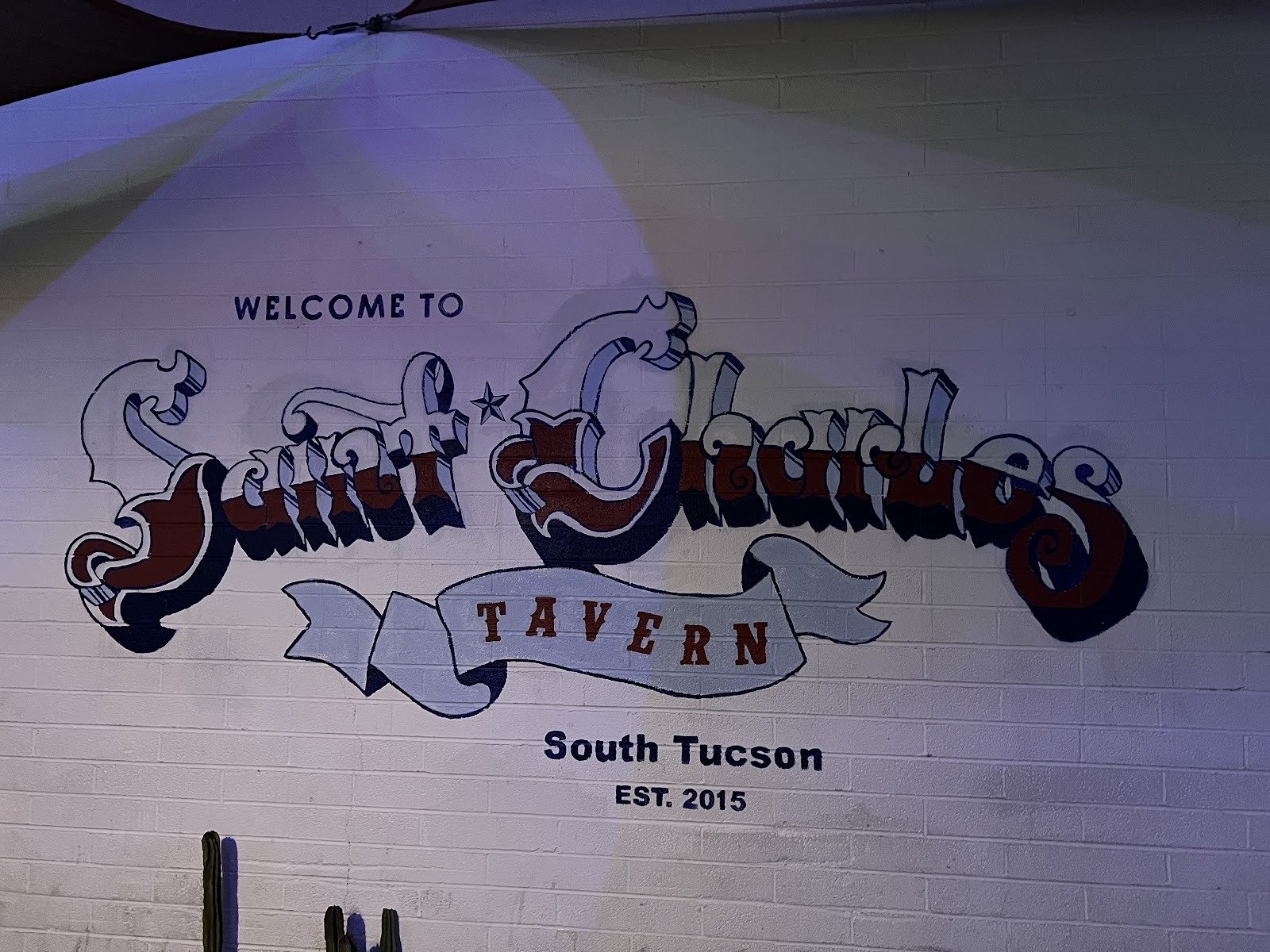 A hand-painted wall mural reading Welcome to Saint Charles Tavern, South Tucson, Est. 2015.